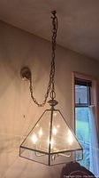 Hanging pyramidal brass and glass light fixture with four candle-style bulbs and chain suspension.