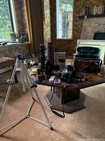 Photo showing tripod set up in room with items on table in background including camera, lenses and book.