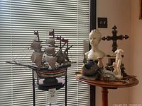 Wooden ship model with sails, busts and other decorative items on round table by window