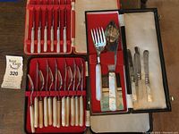 Overview of multiple pieces of silver plate cutlery and serving utensils with mother of pearl handles from the lot, displayed in boxes on a table.