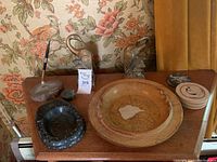 Photo showing all items on wooden surface with floral wallpaper background: soapstone ashtray, large ceramic ashtray, coasters, brass swan bookends, geode pen holder with pen.