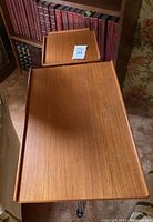 Top view of teak table featuring the built-in tray extended showing wood grain and size relative to books and chair.