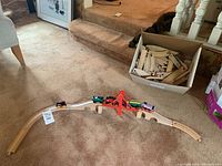 Wide view of the assembled train track on carpet with red bridge and four train cars displayed. Box of additional track pieces in background.