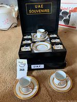 Open black presentation box showing 12 espresso cups and 12 saucers neatly arranged, with two cups and saucers placed outside the box for display.