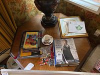 Overview of lot with books, tea cup and saucer, framed certificates, and small collectibles on wooden table.