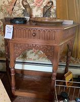 Side view of wood side table showing carved floral and arch designs, turned legs, and lower shelf.