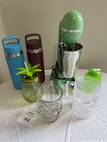 All items in lot arranged on table: milkshake maker, two metal water bottles, skull glasses, pineapple glass jar