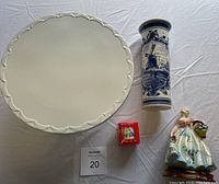 Top-down photo of white Cake Boss cake plate, blue Delft Blue vase, boxed Bunnykins egg cup, and Italian lady figurine on white cloth background