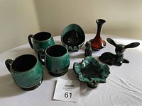 Photo showing all items on a table, three mugs, leaf-shaped ashtray, leaf dish, orange vase, deer and dog figurines.