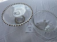 Photo showing both the cake platter and fruit bowl side by side on a white tablecloth, highlighting the beaded rims and pedestal base of the platter.