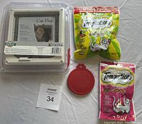 Lot contents with cat flap, two bags of Temptations treats and red food can cover all laid out on white background