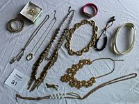 Multiple assorted costume jewellery including various necklaces, bracelets, bangles, and chains placed on a white sheet.