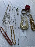 Wide view of assorted costume jewelry laid out on white cloth including necklaces, bracelets, and rings.