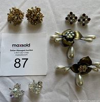 Photo showing six pairs of assorted clip-on earrings including gold rhinestone clusters, pearl floral designs, and cubic crystal styles.