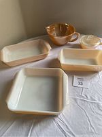 Photo of five Fire-King glass dishes: one square, two rectangular, one mixing bowl with handle and spout, and one small lidded bowl on a white tablecloth.