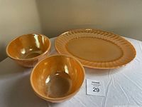 Two butterscotch-colored Fire-King mixing bowls and one large Anchor Hocking platter displayed together on a table.