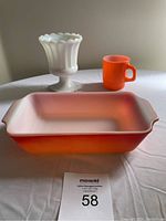 Photo showing all three items: Fire-King orange square casserole, orange mug, and small white milk glass planter on a table.