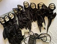 Nine Halloween pathway markers with skeletal skull faces, black hooded cloaks, and plastic lawn stakes arranged on a flat surface. Nearby is a black strobe light with attached cables and plug.