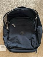 Front view of navy blue Kipling backpack with main zipper compartment, front zipper pocket, side pockets, and Kipling round logo patch in matching navy blue.