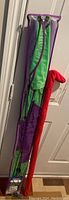Folded nylon biplane kite stored vertically showing green and purple other than a red tube case.