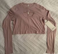 Full view of light pink long sleeve crop top laid flat on white textured background, tag visible on sleeve.