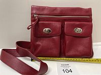 Front side view of the red Danier leather purse placed upright showing zipper pull and two front pockets with silver turn-locks, measuring about 8 inches wide indicated by a ruler.