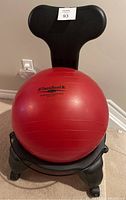 Front view of red TheraBand professional exercise ball seated on the black fit chair with contoured backrest and caster wheels.
