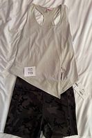 Beige tank top laid flat over forest camo shorts with tags visible showing they are new or unused.
