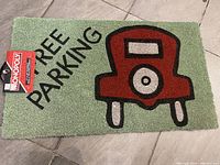 Green welcome mat with Monopoly Free Parking design, showing red car and black text 'FREE PARKING'