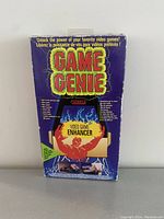 Frontal view of the Game Genie box showing logo, product illustration and feature texts