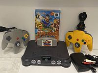Front angle showing Japanese Nintendo 64 console with gray and yellow controllers, Diddy Kong Racing cartridge and box, power adapter and AV cables.