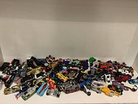 Photo showing a pile of assorted Hot Wheels cars in different colors and styles on a white shelf.