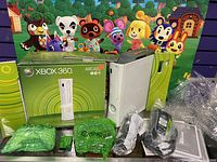 White Xbox 360 console with original green circular themed box and several plastic wrapped accessories on a table.