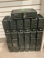 Thirteen original Xbox consoles stacked together against a wall, showing front ports and power buttons.