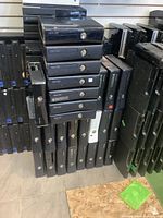 Stack of Xbox 360 Slim consoles in black and white, arranged in rows and columns on floor and shelves.