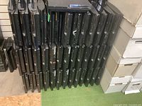Multiple PlayStation 3 consoles stacked in rows showing the front and top, displaying black slim console shells with varying wear and marks.