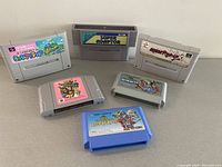 Lot of six Nintendo cartridges and one adapter chip on beige surface.