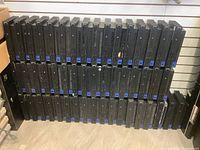 Wide view of two shelves filled with black Sony PS2 Fat consoles, showing front panels with vents and disc trays.