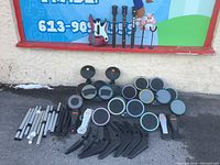 5 top drum sets with pads and colored rims, various poles, foot pedals, and stands arranged outdoors on pavement