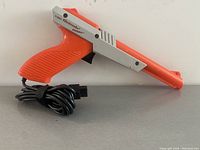 Image showing side view of orange and gray Nintendo Zapper light gun controller with USB style cable coiled underneath.