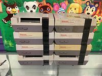 Front view of stacked eight NES consoles showing varying discoloration and missing cartridge door on one unit.