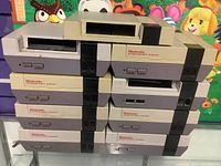 Stacked lot of 12 Nintendo NES consoles showing front and top sides.