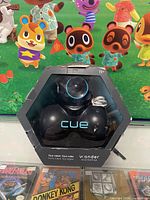 Front view of Wonder Workshop Cue black robot in original packaging showing the device and cable inside with clear hexagonal plastic cover.