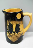 Front side of the jug showing two black silhouettes of owls on a branch against a black and yellow glazed background with a yellow circular moon above.