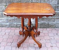 Full view of antique East Lake parlor table showing carved legs, casters, and wood top.