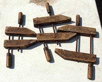 Four antique wooden clamps arranged flat showing front view with wooden handles and metal rod adjusters.