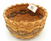 Side and top view of a round hand woven basket with natural and darker wood strips, showing detailed weaving pattern at rim and base.
