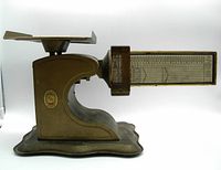 Side view of vintage Pelouze postal scale showing weighing platform, curved metal base, and detailed horizontal measurement bar with weight and postal rate graphics.