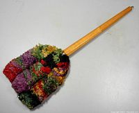 Side angled view showing the full length wooden handle and large multi-colored yarn mop head.