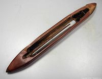 Top view of the large handcarved wooden weaving shuttle showing elongated oval shape and hollow interior for bobbin.